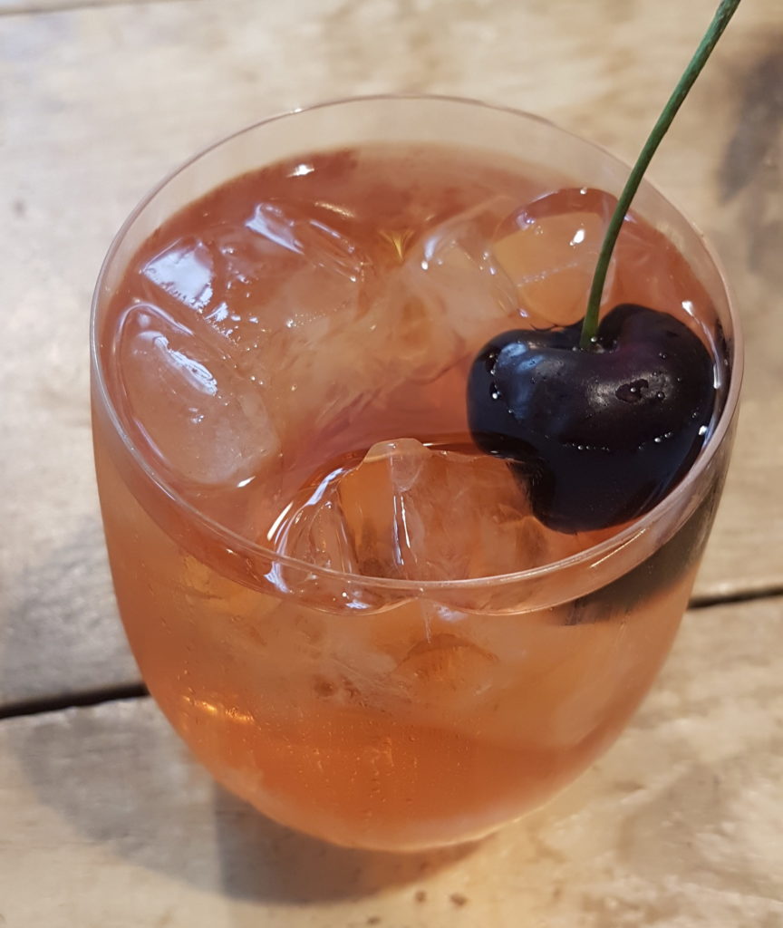 glass of assam mangalam iced tea with a cherry in it